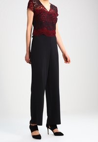 Bordeaux kanttop met een V-hals en kapmouwen, gecombineerd met brede zwarte broek. Zwarte hoge hakken maken de look compleet.
