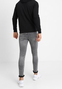 Jeans grigi aderenti con texture sbiadita, risvoltini e tasche posteriori, abbinati a una felpa nera con cappuccio e scarpe da ginnastica bianche.