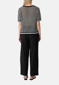 Zwart-wit gestreepte gebreide top met korte mouwen, gecombineerd met zwarte, lose, gekreukte broek en zwarte platte sandalen.