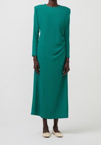 Abito a maniche lunghe, di colore teal, con tessuto testurizzato, scollatura rotonda e drappeggio laterale. Design lungo fino al pavimento con una vestibilità comoda e dettagli minimi.