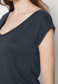 Camiseta V de gola cinza escuro com mangas curtas, feita de um tecido suave, apresentando uma textura lisa e um design ajustado. Sem padrões ou detalhes visíveis.