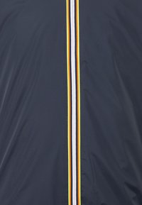 Granatowa kurtka z pionowym zamkiem błyskawicznym z paskami w kolorach białym, żółtym i pomarańczowym; wykonana z gładkiej, lekkiej tkaniny.