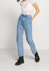 Jeans en denim bleu clair taille haute avec une coupe droite, dotés de cinq poches et de bords effilochés, associés à des bottes noires à lacets.