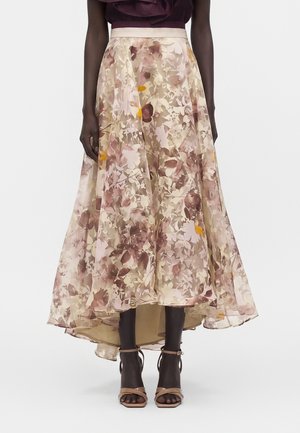 Jupe midi à imprimé floral effet high-low en tons beige, rose et marron, portée avec des talons nus à bride à la cheville sur un mannequin à la peau foncée.