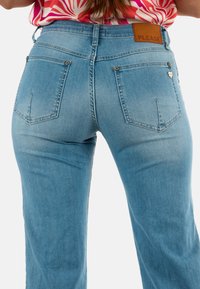 Jeans de mezclilla azul claro con un diseño de talle alto, dos bolsillos traseros y una etiqueta de cuero con la palabra "PLEASE" en la cintura.
