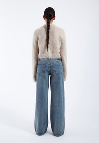 Fuzzy beige sweater with long sleeves paired with wide-leg blue denim jeans. The ensemble features a relaxed fit and minimal detailing.