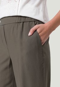 Vaatteet, joissa on joustava vyötärö, oliivinvihreänä. Valmistettu pehmeästä kankaasta, joissa on sivutaskut ja väljä istuvuus. Sileä pinta ja minimaalinen saumatus.