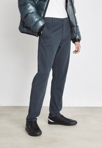 Pantalones de algodón azul oscuro, de corte recto, con cierre de botón, combinados con una chaqueta acolchada brillante y zapatillas negras con un acento de color.