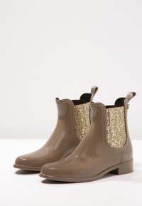 Botas de lluvia con un acabado taupe brillante, que presentan un panel de purpurina dorada a cada lado, un tacón bajo y tiradores para ponerlas fácilmente.