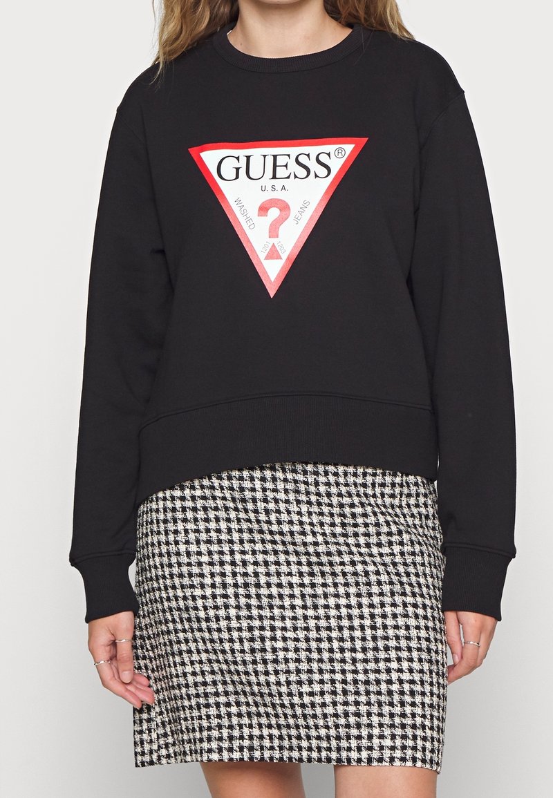 Sudadera negra con un gran diseño de logo triangular en rojo y blanco, combinada con una falda de patrón jaqués en blanco y negro.