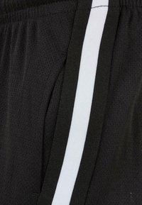 Black athletic shorts featuring a textured fabric, side pockets, and a vertical white stripe along the outer seam.