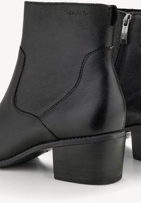 Botas de tobillo de cuero negro con textura suave, que cuentan con un cierre de cremallera lateral, costuras curvadas y un diseño de tacón grueso.