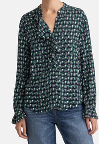 Blusa a maniche lunghe color navy con un motivo circolare verde e bianco. Presenta un colletto arricciato e chiusura con bottoni, realizzata in tessuto leggero.