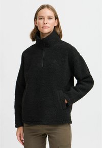 Black fleece pullover with a high collar, half-zip closure, and side pockets. Textured, soft fabric with a relaxed fit.