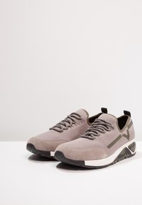 Szare buty sportowe z siateczkową cholewką, zamszowymi wstawkami, grubą białą śródpodeszwą i teksturowaną czarną gumową podeszwą. Sznurowadła w kontrastowym kolorze.