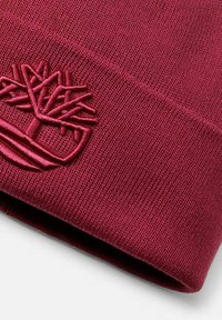 Cappello di tessuto lavorato a maglia bordeaux con orlo piegato, caratterizzato da un logo ad albero ricamato nello stesso colore del filato.