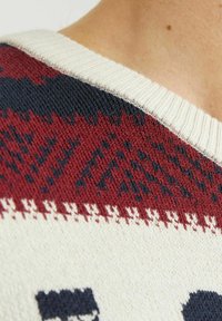 Pull en tricot avec un col côtelé crème, ornée de motifs géométriques rouges et marine sur un fond texturé.