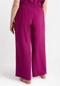 Spodnie typu wide-leg w jaskrawym magencie, z elastycznym fasonem w talii. Miękki materiał układa się łatwo, ma gładką fakturę i minimalistyczny design.