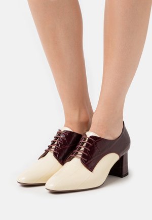 Chaussures en cuir bicolores avec une finition vernissante bordeaux et crème, présentant un motif texturé et un talon carré. Lacets sur le dessus.