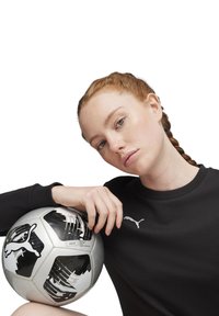 Zwarte sweatshirt met geribbelde halslijn, voorzien van een wit Puma-logo, die een zilveren en zwart patroon voetbal vasthoudt met duidelijke graphics.