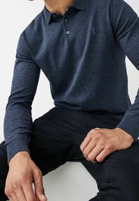 Marineblaues Langarm-Polohemd aus strukturiertem Stoff, ausgestattet mit einer Zwei-Knopf-Leiste und einem dezenten Logoakzent auf der Brust.