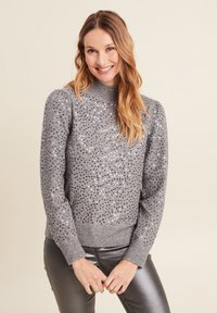 Grauer Strickpullover mit hohem Kragen, verziert mit silbernen Pailletten, mit gerippten Bündchen und Saum, getragen mit glänzenden grauen Hosen.