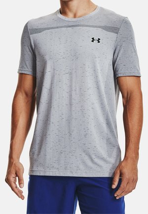 Homme portant un t-shirt de sport à manches courtes gris clair avec un logo Under Armour noir et un short bleu sur fond blanc.