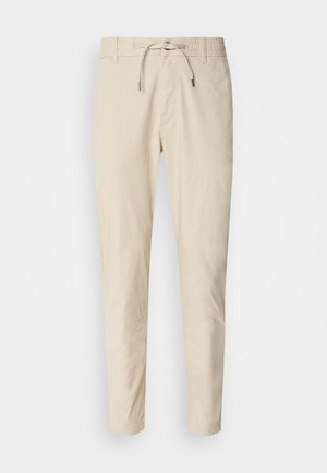Pantalones beige claros con una textura de tela suave, cinturilla elástica y cordón ajustable. Diseño de pierna ajustada. Sin patrones visibles.