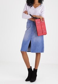 Džínová sukně s předním rozparkem, zkombinovaná se světle fialovým topem s dlouhým rukávem. Červená texturovaná psaníčko a černé kotníkové boty dokreslují tento vzhled.