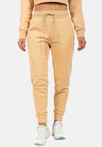 Beige sweatpants met een elastische tailleband, een trekkoord en taps toelopende benen. Zacht materiaal en geribbelde manchetten. Minimale merkbedrukking aan de zijkant.