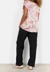 Blouse à manches courtes, crème avec imprimé paisley rose, associée à un pantalon cargo noir et des ballerines beiges. L'ensemble présente une coupe décontractée et des poches.
