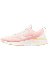 Zapatilla de running Nike de color rosa claro con logo swoosh blanco, suela blanca con acentos amarillos y parte superior de malla transpirable.
