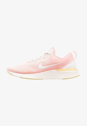 Baskets de course Nike rose clair avec logo swoosh blanc, semelle blanche avec accents jaunes et tige en mesh respirant.