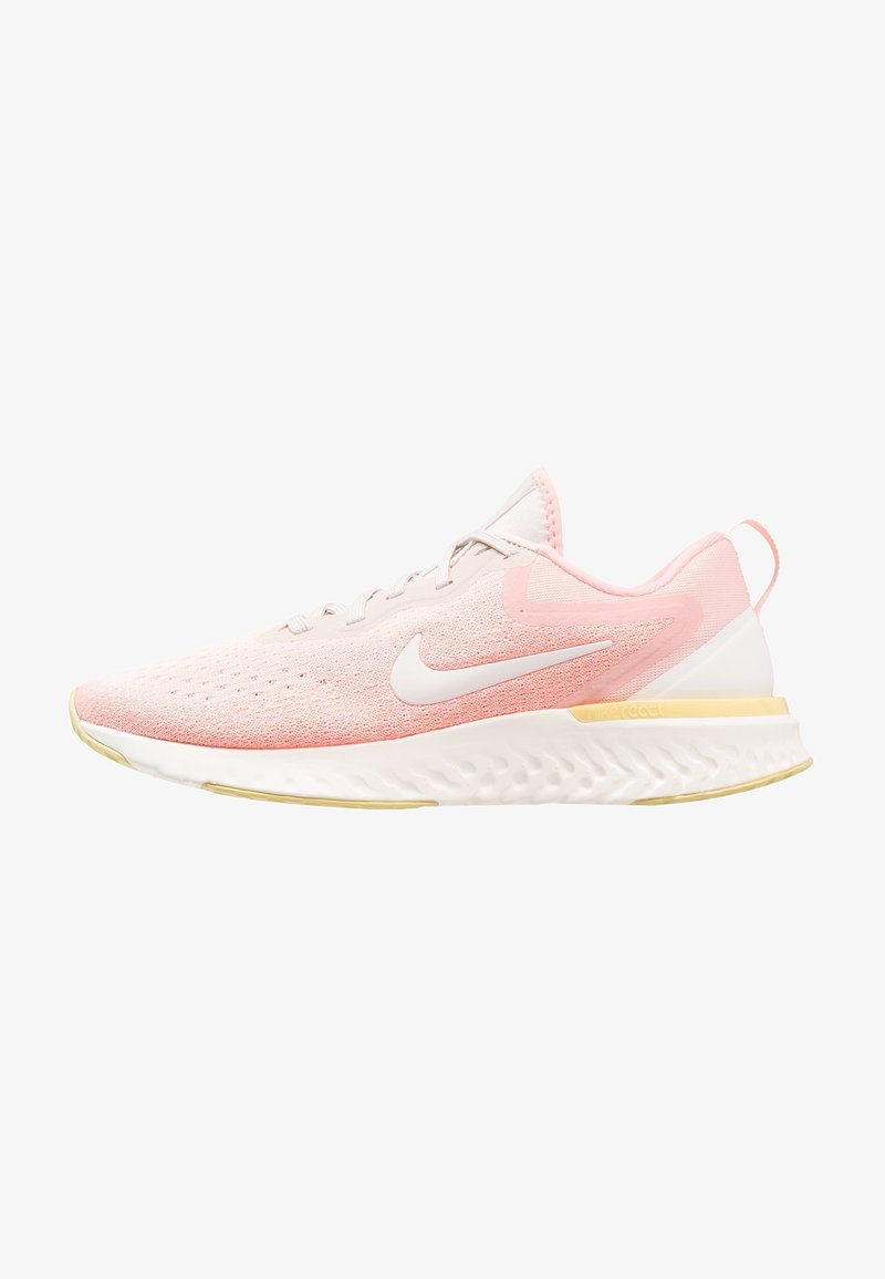 Světle růžová běžecká obuv Nike s bílým logem swoosh, bílou podrážkou se žlutými akcenty a prodyšným síťovinovým svrškem.