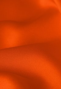 Tissu satin orange vif avec une texture lisse et brillante, présentant des variations subtiles d'ombre et de profondeur à travers les plis.