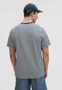 T-shirt rayé en coton bleu marine et blanc, avec un col rond et des manches courtes. Coupe décontractée, associé à un short bleu clair et une casquette.
