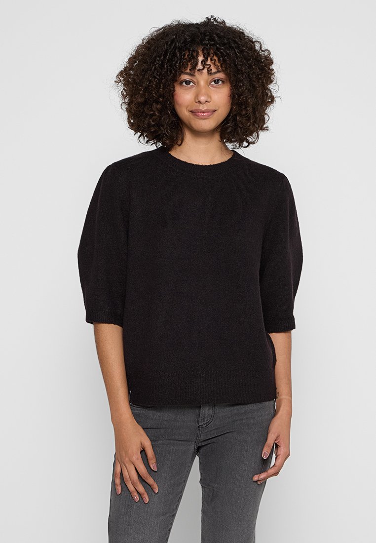 Zwarte gebreide trui met een ronde halslijn, korte poefmouwen en een zachte textuur. Gecombineerd met grijze jeans, minimalistisch ontwerp.