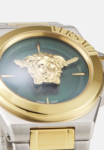 Versace laikrodis su auksinės spalvos rėmeliu, žalia ciferblatu, kuriame yra centrinė auksinė Medūzos galva, ir sidabro nerūdijančio plieno apyranke.