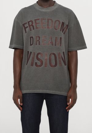 Szara, oversize'owa koszulka wykonana z miękkiej bawełny, z wyraźnym, wyblakłym napisem "FREEDOM DREAM VISION" w ciemnobrązowym kolorze na przodzie.
