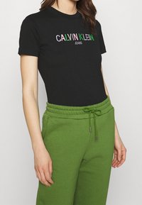 Černé bavlněné tričko s výšivkou "CALVIN KLEIN JEANS" v několika barvách. V kombinaci se zelenými tepláky s páskem na stažení.