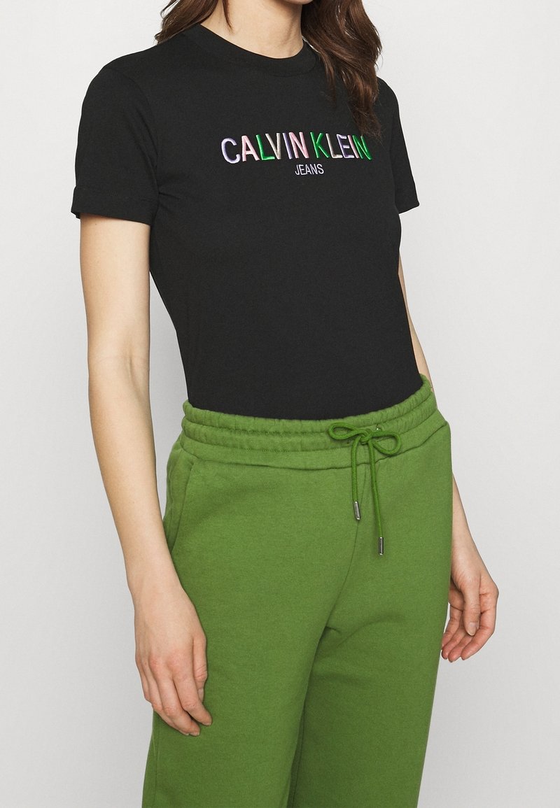 Černé bavlněné tričko s výšivkou "CALVIN KLEIN JEANS" v několika barvách. V kombinaci se zelenými tepláky s páskem na stažení.