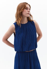 Top senza maniche blu con un motivo testurizzato e ondulato, realizzato in tessuto leggero. Caratterizzato da un collo rotondo e una silhouette ampia.