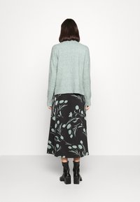 Světle zelený pletený svetr s kulatým výstřihem, ve spojení s černo-květinovým maxi šaty s tyrkysovými akcenty a kotníkovými botami.