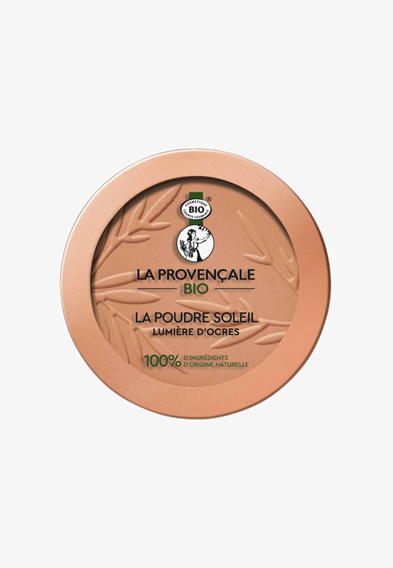Compact rond en or rose avec un design de feuille texturé, comportant le nom du produit en noir et vert, ainsi qu'un texte indiquant des ingrédients naturels.