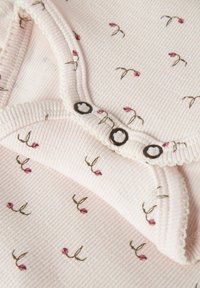 Tissu en rib pourpre clair avec un petit imprimé floral ; présente un col rond avec des garnitures en dentelle et des boutons décoratifs en noir et blanc.