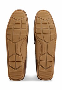 Scarpe con suola in gomma marrone e finitura testurizzata. La suola presenta un motivo geometrico per la trazione e un logo del marchio in rilievo.