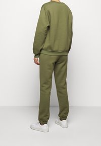Olivgrön sweatshirt och joggers i mjuk tyg, med ribbade muddar och midjeband, tillsammans med vita sneakers.