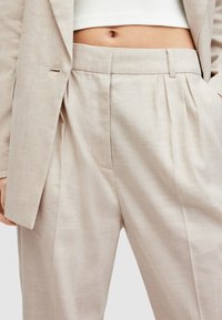Beige linnenbroek met een hoge taille, een geplooide voorkant en zijzakken; gecombineerd met een cropped witte top en een textuurstof.