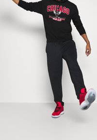 Sweatshirt noir avec le logo "Chicago Bulls" en rouge, associé à un pantalon de survêtement noir. Chaussures de sport rouges avec accents noirs et semelles blanches.