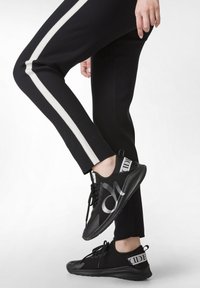 Zwarte sportbroek met witte zijkanten, gecombineerd met zwarte sneakers met een metallic logo en een ondersteunende, textuurgegeven zool.